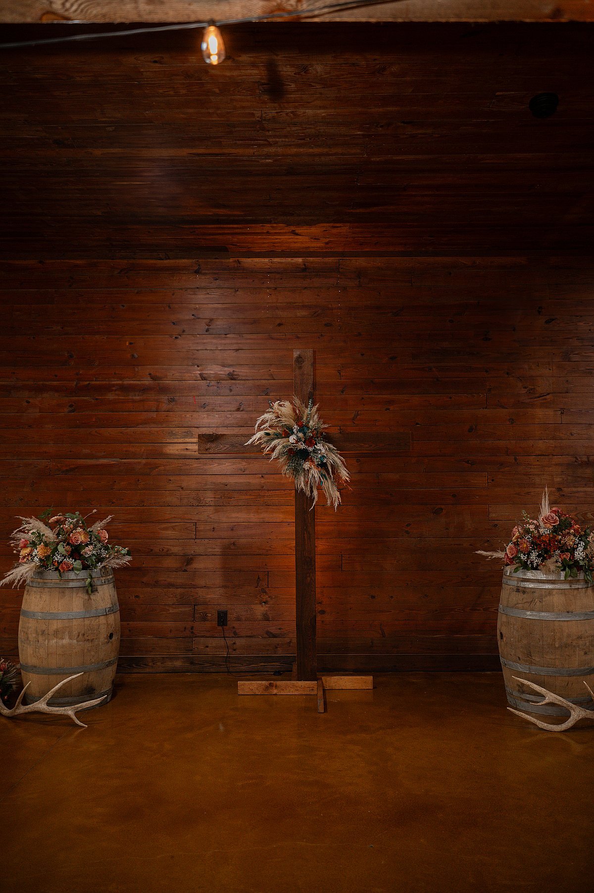 Rustic wooden cross ceremony altar with barrel flower arrangements inside barn