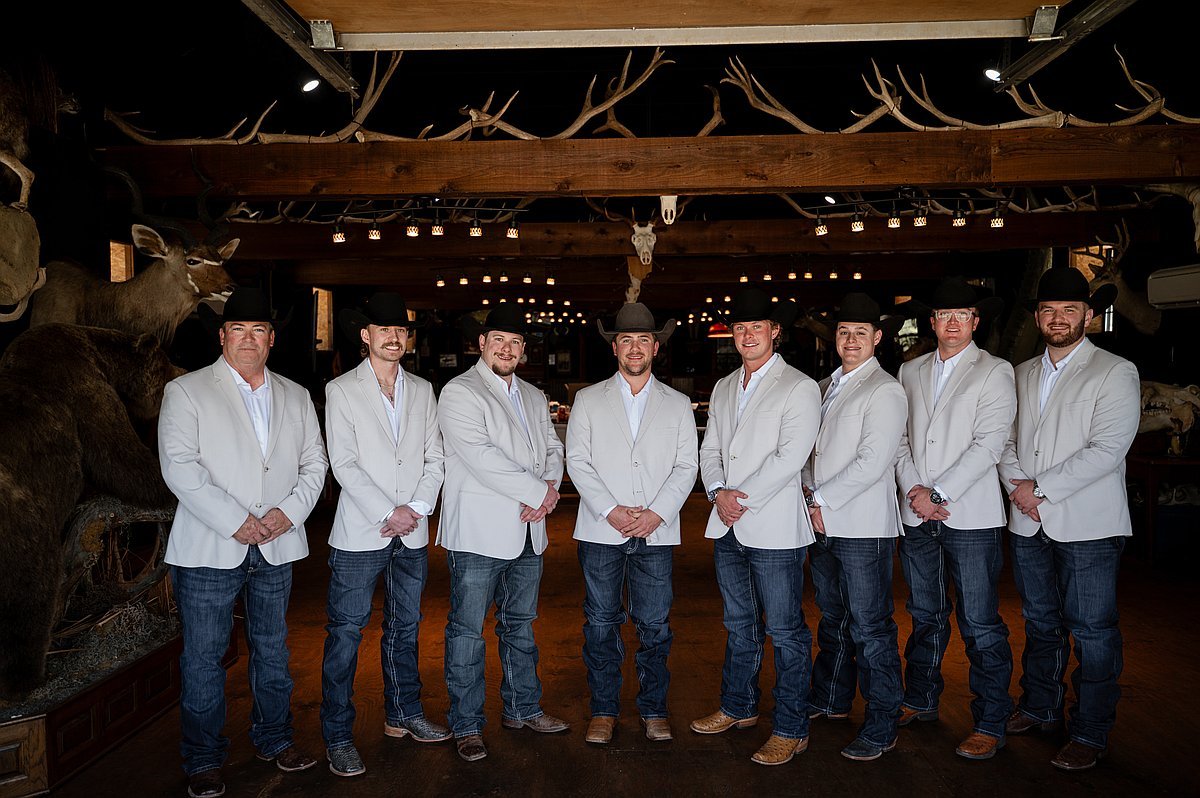 Groomsmen in white jackets and cowboy hats posed in rustic barn interior